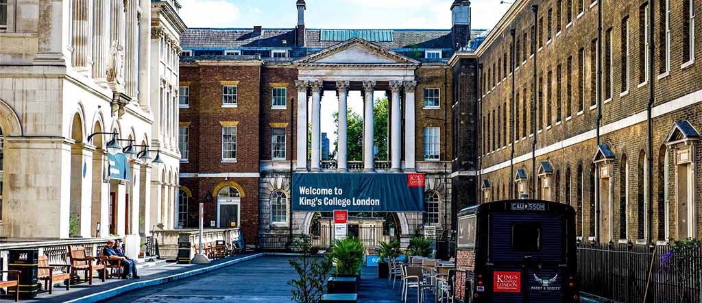 Kings College London main building with a college bus parked outside having kings college logo on it 